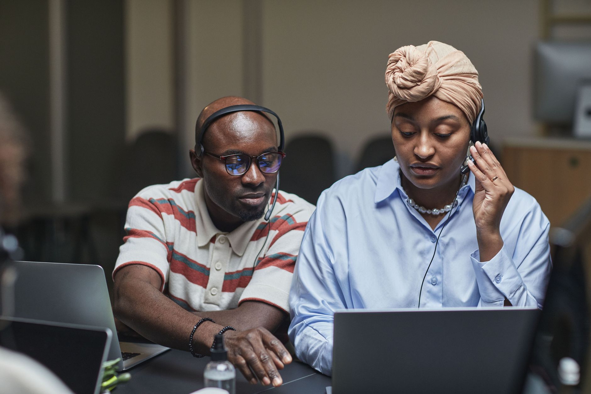 Dois colegas de trabalho usando fones de ouvido e laptops em um escritório moderno, em discussões de trabalho.