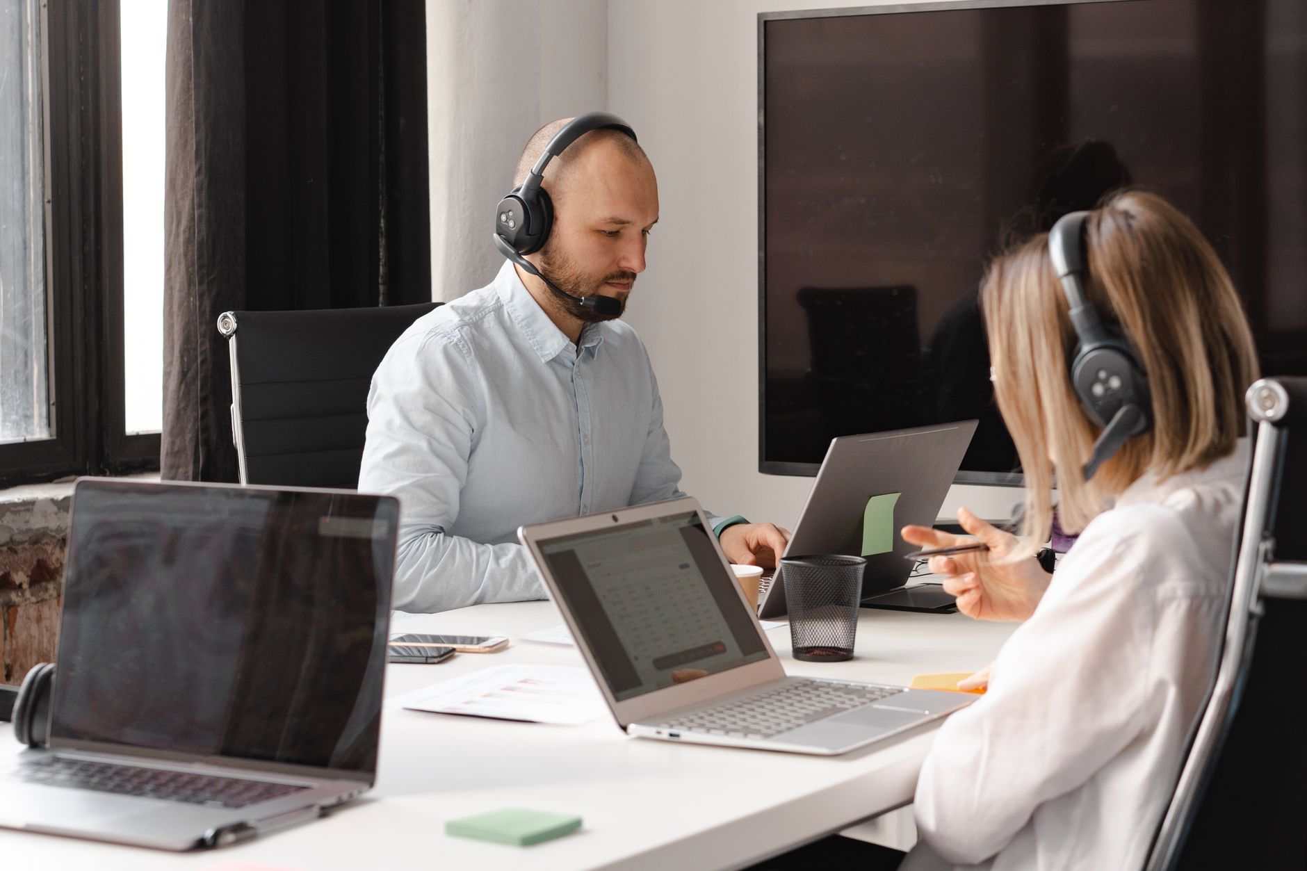 Agentes de suporte ao cliente trabalhando juntos com laptops e fones de ouvido em um escritório.