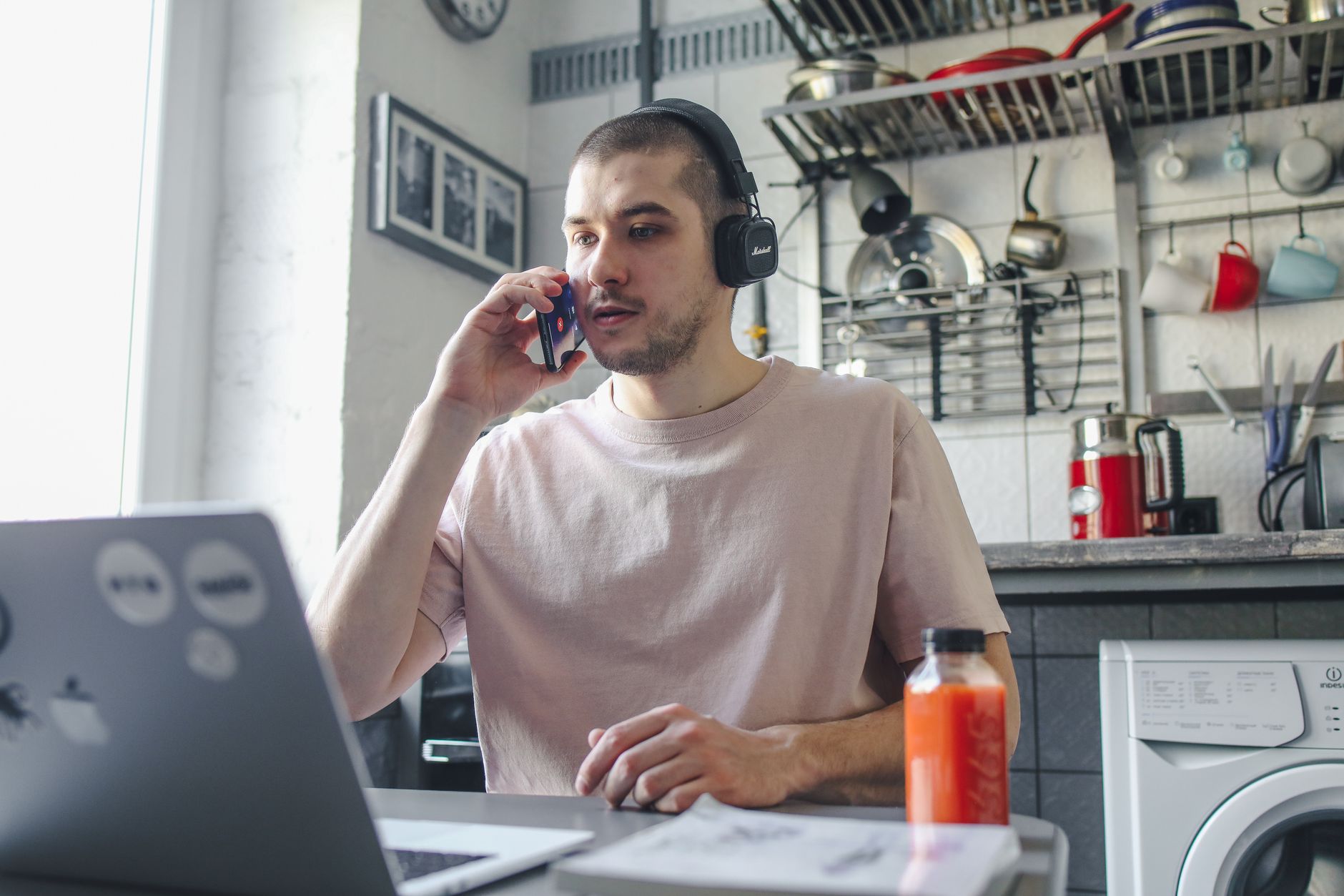 Homem adulto fazendo múltiplas tarefas em casa com laptop e celular, em um ambiente confortável.