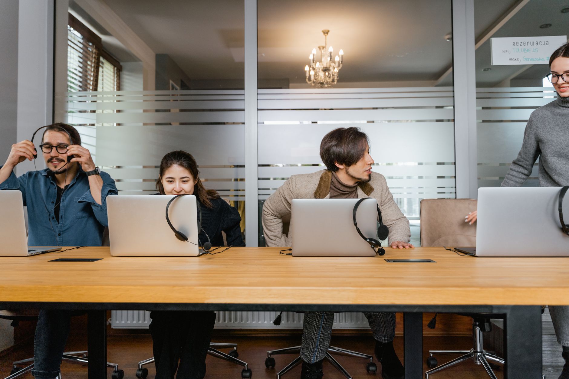 Profissionais em um escritório trabalhando com laptops e fones de ouvido, em um ambiente de equipe.